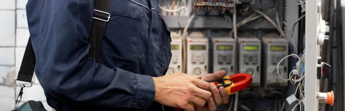 Electrician engineer checks electrical circuit in control panel for high current and voltage, starting and commissioning relays for industrial production.