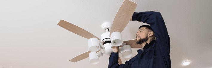 Electrician repairing ceiling fan with lamps indoors.