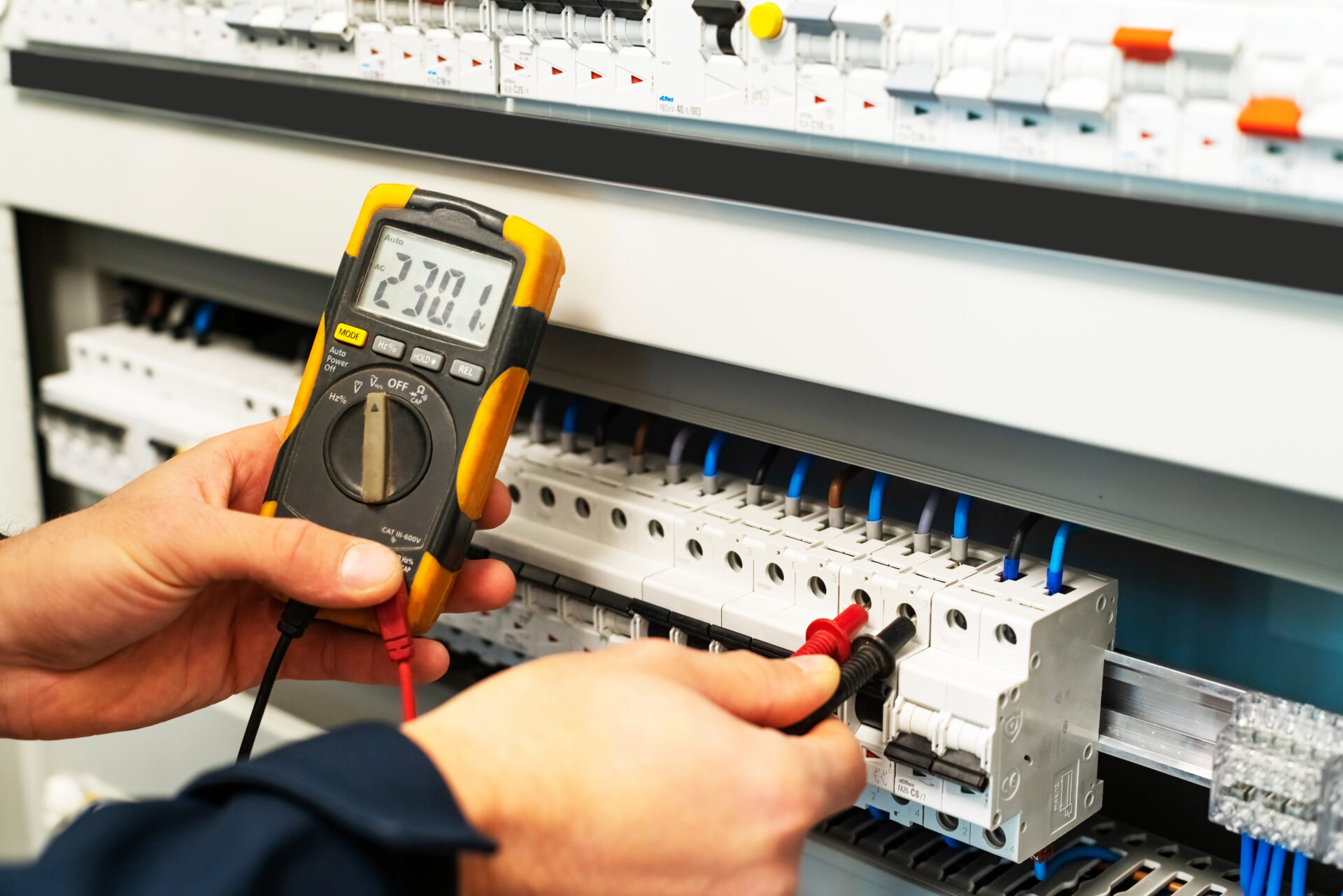 A male electrician who is testing the voltage in the switchboard